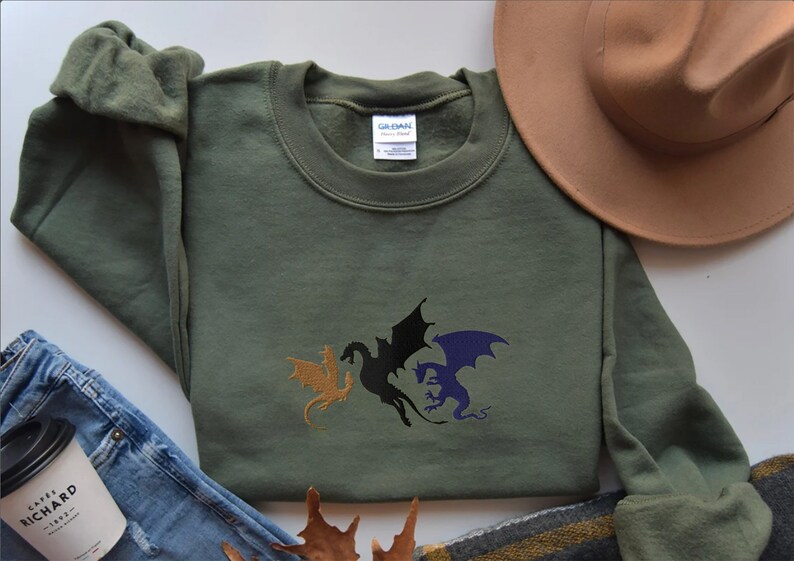 May include: A green sweatshirt with a three-headed dragon design embroidered on the front. The dragons are gold, black, and purple.