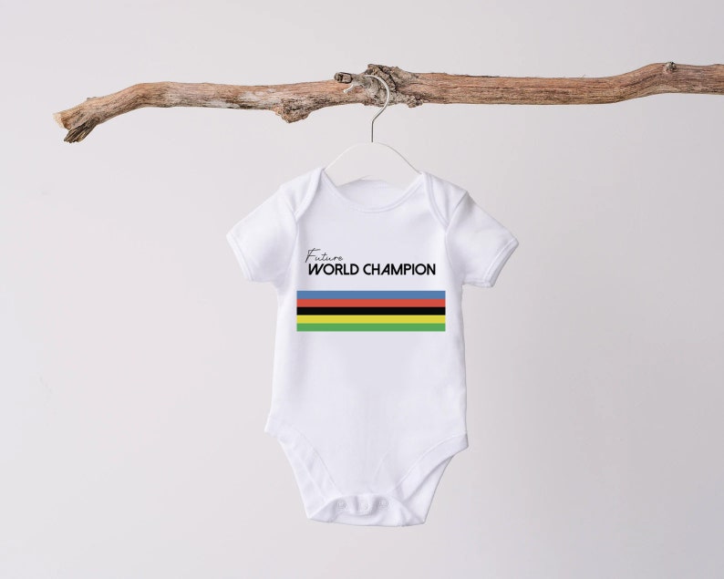K&ouml;nnte beinhalten: Ein wei&szlig;er kurz&auml;rmeliger Babybody mit dem Schriftzug Future WORLD CHAMPION in schwarzen Buchstaben &uuml;ber einem horizontalen Streifenmuster in den Farben Blau, Rot, Schwarz, Gelb und Gr&uuml;n. Das Kleidungsst&uuml;ck hat einen Rundhalsausschnitt und Druckkn&ouml;pfe.