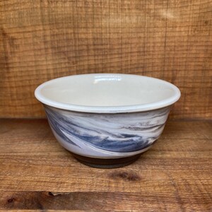 May include: A small white ceramic bowl with a marbled design in shades of gray and brown. The bowl has a slightly rounded bottom and a smooth, glazed surface.