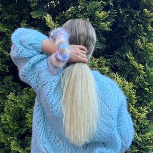May include: A light blue knitted sweater with a delicate openwork pattern. The sweater has a loose fit and long sleeves.