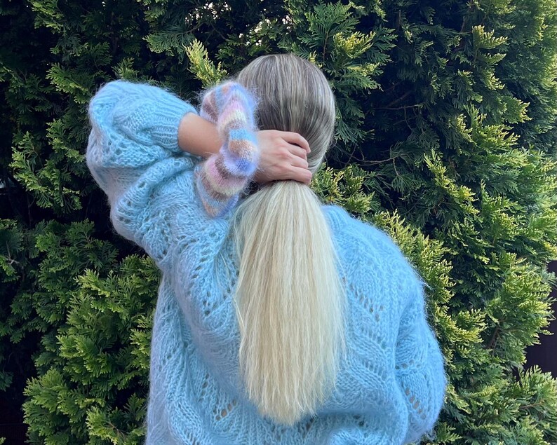 May include: A light blue knitted sweater with a delicate openwork pattern. The sweater has a loose fit and long sleeves.