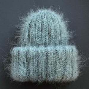 May include: A soft, light blue beanie hat with a fuzzy texture. The hat is knitted with a ribbed brim and a slightly slouchy crown. The hat is made of a fluffy, possibly mohair or angora yarn, and is suitable for cold weather.