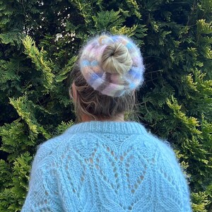 May include: A person wearing a light blue fuzzy sweater with a colorful knit hair scrunchie.