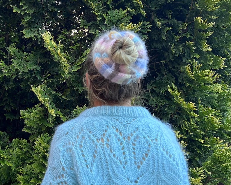 May include: A person wearing a light blue fuzzy sweater with a colorful knit hair scrunchie.