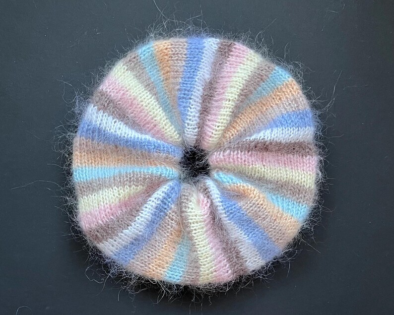 May include: A fluffy, multi-colored striped knit hair scrunchie in shades of pink, blue, and brown.