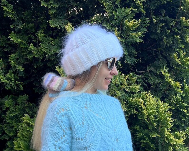 May include: A white fuzzy knit hat with a light blue sweater and a colorful knit hair tie.