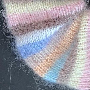 May include: Close-up of a soft, fuzzy knit fabric with a multi-colored striped pattern in shades of pink, white, blue, brown, and peach.
