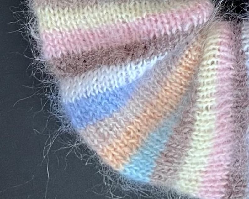 May include: Close-up of a soft, fuzzy knit fabric with a multi-colored striped pattern in shades of pink, white, blue, brown, and peach.