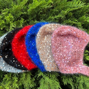 May include: Five knitted hats with sequins in different colors: gray, black, red, blue, and pink. The hats are arranged in a row, with the gray hat on the left and the pink hat on the right.