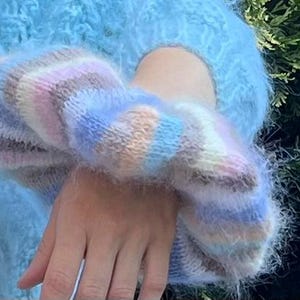 May include: A fluffy blue sweater with a colorful striped cuff. The cuff is made of a soft, fuzzy yarn and has a light blue, pink, and brown color scheme.