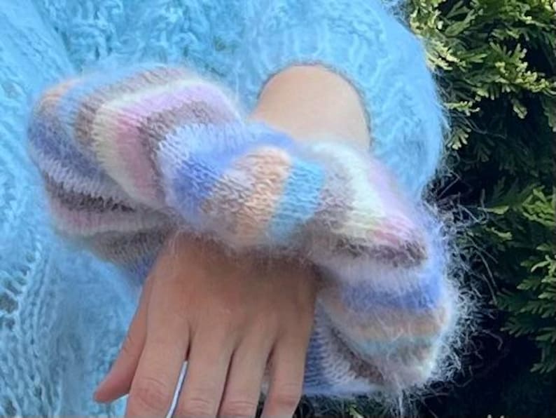 May include: A fluffy blue sweater with a colorful striped cuff. The cuff is made of a soft, fuzzy yarn and has a light blue, pink, and brown color scheme.