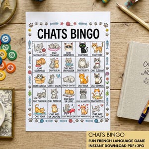 May include: A printed "Chats Bingo" game sheet with cat illustrations and French vocabulary. The sheet features a grid of cat-themed images and words, with the title "Chats Bingo" at the top. A notebook and pencil are visible.