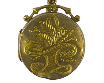 Könnte beinhalten: Ein goldenes Medaillon mit einem gravierten Blumenmuster auf der Vorderseite. Das Medaillon hat einen Klappdeckel und eine Schlaufe zum Anbringen einer Kette.