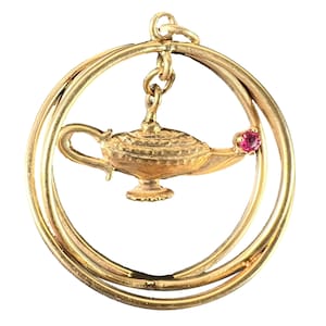 May include: A gold pendant with a genie lamp charm hanging inside two interlocking circles. The lamp has detailed features and a small red gemstone is set into the circle. The pendant is likely made of gold.