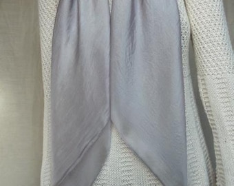 Puede incluir: Una bufanda de color gris claro liso con una textura suave y ligeramente reflectante colocada sobre un suéter de punto color crema de manga larga, con un sutil patrón de canalé vertical y cuello redondo.