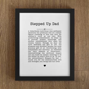 May include: A framed print with the text "Stepped Up Dad" in a black frame. The print features a heartfelt message about a father figure, with a small heart symbol at the bottom. The background is a wooden surface.