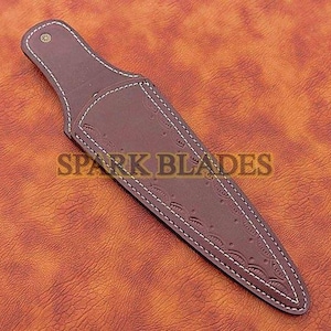 May include: A brown leather knife sheath with white stitching and embossed floral patterns. The sheath has a pointed end and a wide top with a snap closure. The text "SPARK BLADES" is visible on the sheath.