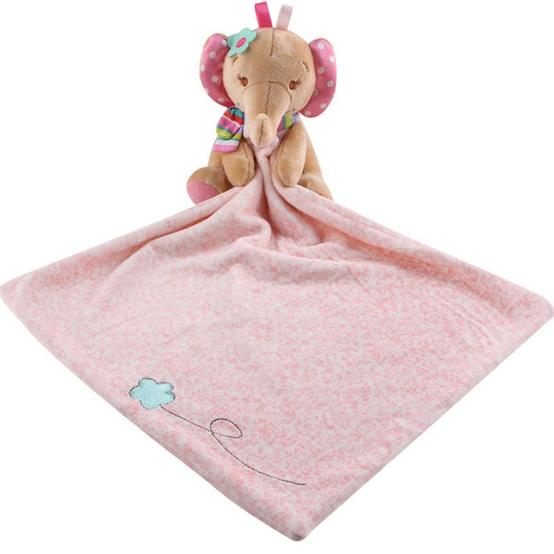 May include: Pink and brown plush elephant with a pink flower on its head, holding a pink and white blanket with a blue flower embroidered on it.