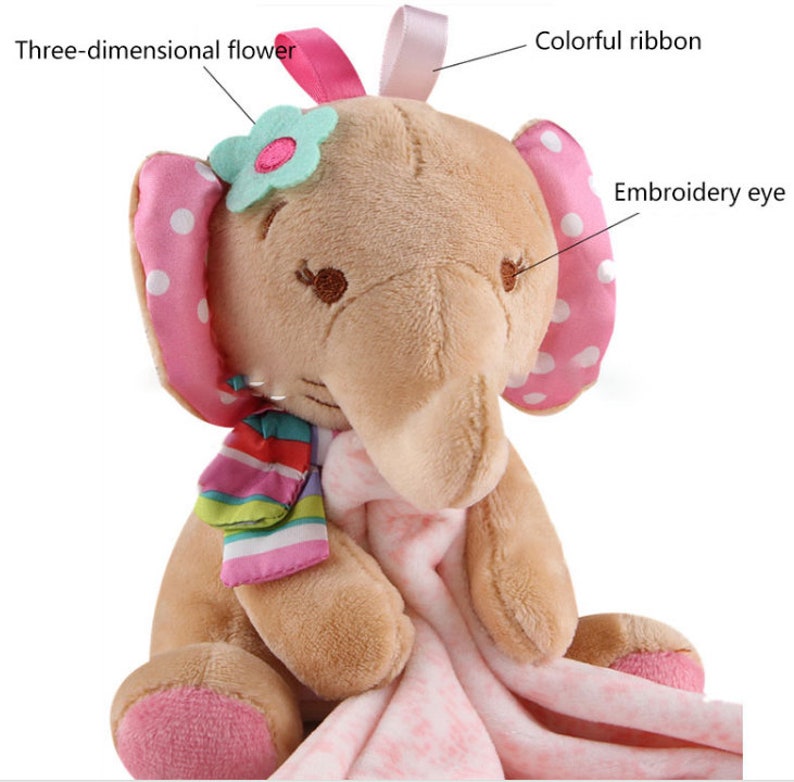 May include: A plush brown elephant toy with pink polka dot ears, a pink ribbon, and a three-dimensional flower. The elephant is holding a pink and white blanket.