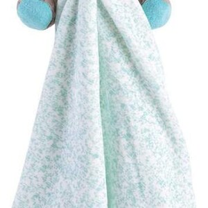 May include: A plush grey donkey toy with blue eyes and a green scarf is attached to a soft, light blue and white blanket with a red flower embroidered on it.