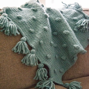 Peut inclure: Une couverture en tricot turquoise avec un point de bobble texturé et des glands sur les bords.