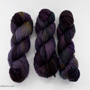 May include: Three skeins of yarn in shades of purple, green, and brown. The yarn is twisted into a rope shape.
