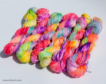 May include: A selection of vibrant yarn skeins in a rainbow of colours, including pink, yellow, orange, purple, and green. The yarn is arranged diagonally, with each skein displaying a gradient of hues. The website moonsilkarts.com is visible.