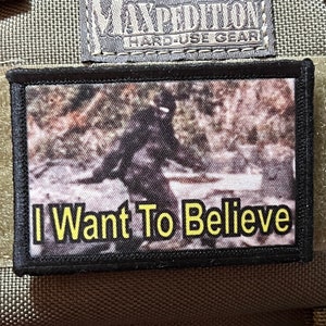 May include: Black patch with a blurry image of a figure in the woods and the text "I Want To Believe" in yellow letters.