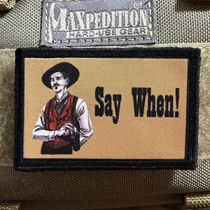 May include: A tan and black embroidered patch with a cartoon image of a man wearing a hat and vest. The text "Say When!" is printed in black on the patch.