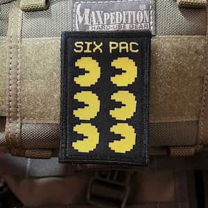 May include: Black patch with yellow Pac-Man characters and the text "SIX PAC" on a green tactical bag.