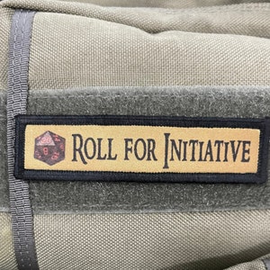May include: A green Maxpedition backpack with a black patch that says "Roll for Initiative" and a black and white patch that says "Maxpedition Hard-Use Gear".