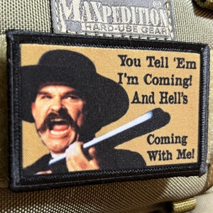 May include: A black and tan embroidered patch with a cartoon image of a man with a mustache and a hat holding a baseball bat. The text on the patch reads "You Tell 'Em I'm Coming! And Hell's Coming With Me!"
