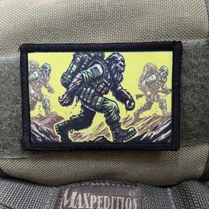 May include: A rectangular patch with a black border shows a cartoon Bigfoot-like figure running on a yellow background. The figure wears military gear and carries a backpack. The patch is attached to green fabric.