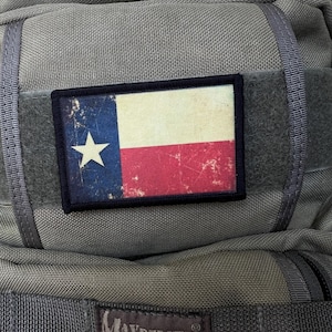 Puede incluir: Una mochila verde Maxpedition Hard Use Gear con un parche de la bandera de Texas desgastado en la parte delantera.
