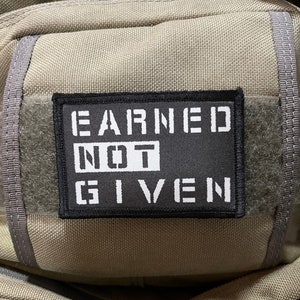 May include: A black and white patch with the text "EARNED NOT GIVEN" on a beige fabric background.