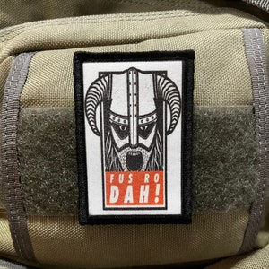 May include: A black and white patch featuring a Viking warrior wearing a horned helmet. The patch has a white background with black outlines and the text "FUS RO DAH!" in red and white.