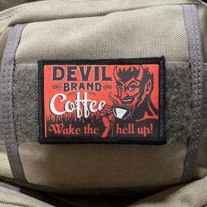 May include: A red and black patch with a cartoon devil holding a coffee cup. The text on the patch reads "Devil Brand Coffee Wake the hell up!"
