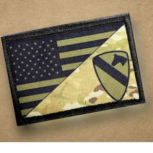 Könnte beinhalten: Ein rechteckiger Aufnäher mit geteiltem Design. Eine Hälfte zeigt die amerikanische Flagge, während die andere ein Tarnmuster und ein Schildemblem aufweist. Der Aufnäher ist mit schwarzen Nähten eingefasst.