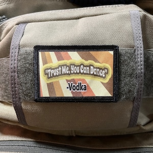 May include: A brown and black patch with a retro design and the text "Trust Me, You Can Dance" -Vodka.