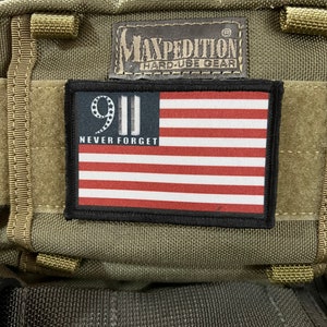 May include: A green Maxpedition backpack with a black patch that says "9/11 Never Forget" and features an American flag.