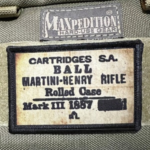 May include: A close-up of a brown and black patch with the text "CARTRIDGES S.A. BALL MARTINI-HENRY RIFLE Rolled Case Mark III 1887" printed on it.
