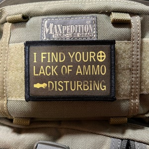 May include: A black and yellow patch with the text "I find your lack of ammo disturbing" on a green tactical backpack.