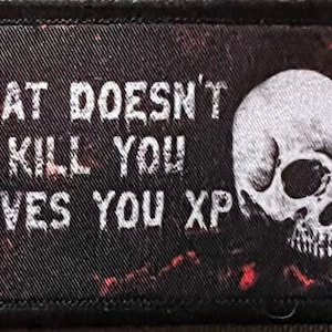 Könnte beinhalten: Schwarzer und roter gestickter Patch mit einem weißen Totenkopf und dem Text "What doesn't kill you gives you XP".