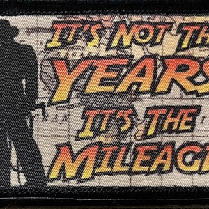 May include: A black and white patch with a silhouette of a person in a hat and the text "It's not the years, it's the mileage" in yellow and orange.