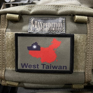 Puede incluir: Una mochila de estilo militar verde con un parche negro que dice "Maxpedition Hard-Use Gear" y un parche más pequeño con un mapa de Taiwán rojo y blanco y el texto "West Taiwan".