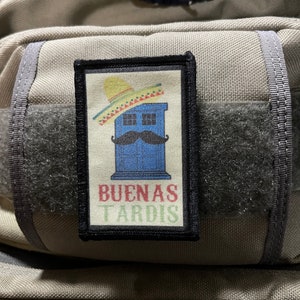 May include: A black and white patch with a blue police box wearing a sombrero and a moustache. The text on the patch reads "Buenas Tardis".