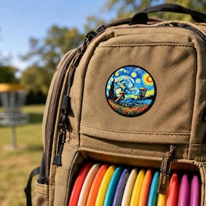 Pode incluir: Uma mochila bege com um autocolante circular que apresenta uma ilustração colorida e rodopiante de uma pessoa a lançar um disco para um cesto de disc golf. A mochila tem um compartimento frontal com uma fila de discos coloridos.