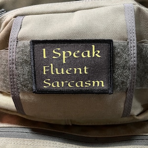 May include: A gray tactical backpack with a black patch that reads "I Speak Fluent Sarcasm".