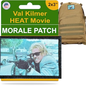 May include: A rectangular morale patch featuring a still from the movie "HEAT" with Val Kilmer. The patch is 2x3 inches and has the text "Val Kilmer HEAT Movie MORALE PATCH". A tan backpack is in the background.