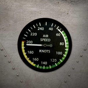 May include: A circular black air speed indicator gauge with white text reading AIR SPEED KNOTS and numbers ranging from 40 to 240. A white needle points to 200, with a yellow arc segment between 200 and 240 and a green arc segment from 60 to 240.